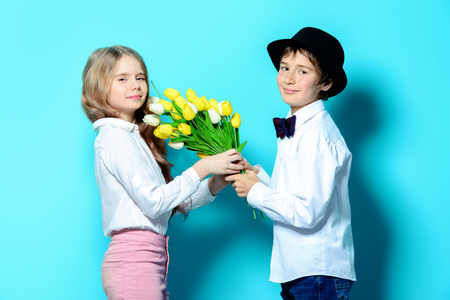 Happy children are posing with a bouquet of spring flowers on blue  background. Happy childhood. Spring holidays.の写真素材