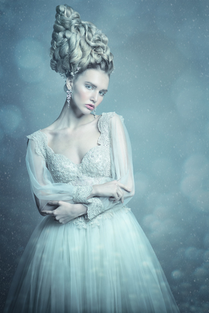 A portrait of a cold beautiful lady wearing a fluffy dress and posing in the studio over the grey background. Beauty,cosmetics, hairstyle, fashion.の写真素材