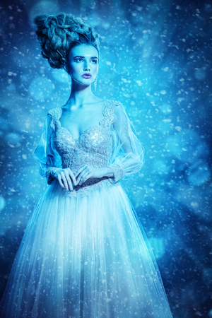 A portrait of a cold beautiful lady wearing a fluffy dress and posing in the studio over the blue background. Beauty,cosmetics, hairstyle, fashion.の写真素材