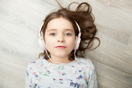 A pretty little girl is lying with headphones on the floor. Fashion home shot. Childhood. Kid's fashion.の写真素材