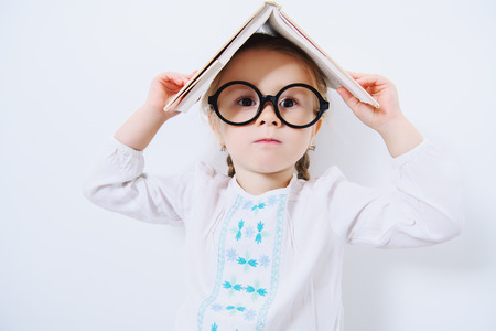 A portrait of a cute pretty girl wearing glasses posing with a textbook over the white background. Beauty, fashion, school, education.の写真素材