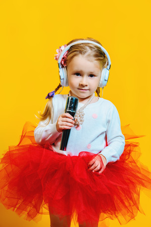 A portrait of a bright young pretty girl in skirt with a microphone. Fashion for kids.の写真素材