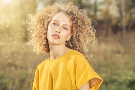 A portrait of a charming young girl with curly fair hair in a yellow dress. Fashion, beauty.の写真素材