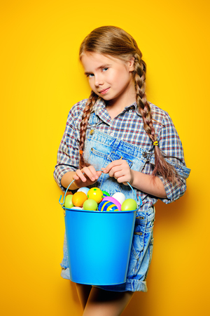 Children's fashion. Cute nine year old girl with long blonde hair is posing in summer clothes with a bucket of easter eggs. Studio shot.の写真素材