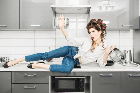 A beautiful girl is wearing everyday clothes in the kitchen on cupboards. Fashion home shot. Pin-up style.の写真素材