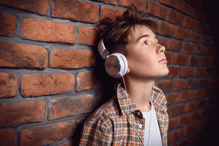 A portrait of a young boy with headphones in casual clothes posing over the brick wall. Fashion for male teenagers.の写真素材