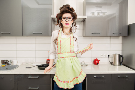 Beautiful young housewife stands in the kitchen. Pin-up style. Fashion home shot.の写真素材