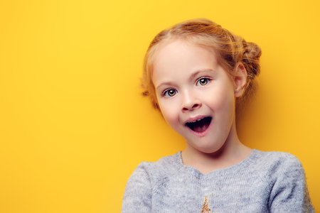 Close-up portrait of a funny emotional girl making faces at camera. Studio shot over yellow background. Childhood concept.の写真素材