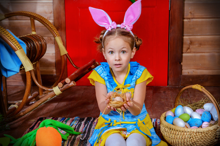 Happy little girl with bunny ears sitting on the porch of a wooden house. Easter holiday. Rural style, easter decoration.の写真素材
