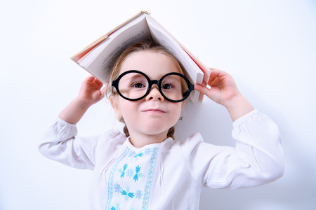 A portrait of a cute pretty girl wearing glasses posing with a textbook over the white background. Beauty, fashion, school, education.の写真素材