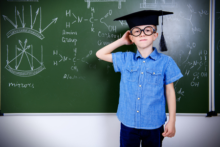 A portrait of a young boy in glasses posing over the blackboard at school. Education, knowledge.の写真素材