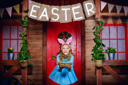Happy little girl with painted eggs is standing on the porch of a wooden house. Easter holidays.の写真素材