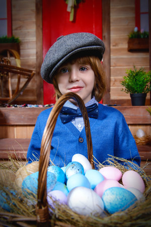 Happy little boy is standing on the porch near the wooden house. Easter holiday. Rural style, easter...