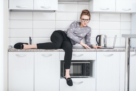 Fashion shot. Beautiful female model is sitting on the countertop of the kitchen set in home clothes. Beauty, fashion.の写真素材