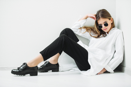 Portrait of a cute girl teenager with sunglasses sitting on the floor in the room. Glasses for a modern young generation. Beauty, fashion.の写真素材