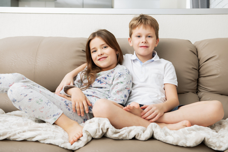 Cute boy and girl are  sitting on the couch.  Fashion home shot. Childhood. Kid's fashion.の写真素材