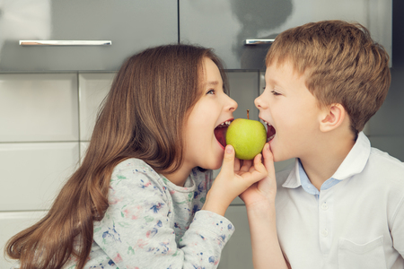 Two cute kids eating an apple in the kitchen. Childhood. Kid's fashion.の写真素材