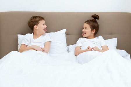 Cute girl and boy lie under the blanket. Family home shoot. Childhood. Kid's fashion.の写真素材