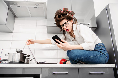 A portrait of a beautiful girl posing in everyday clothes with curlers in her hair with a laptop and a mobile. Fashion home shot. Pin-up style.の写真素材