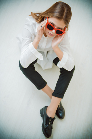 Portrait of a cute girl teenager with sunglasses sitting on the floor in the room. Glasses for a modern young generation. Beauty, fashion.の写真素材