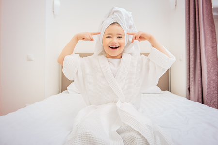 A cute girl is sitting in bathrobe at bed at home. Fashion home shot. Childhood. Kid's fashion.の写真素材