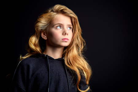 A close-up portrait of a cute emotional girl posing over the black background in studio. Beauty, fashion for kids and teenagers.の写真素材