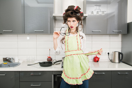 Beautiful young housewife stands in the kitchen. Pin-up style. Fashion home shot.の写真素材
