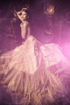 A full length portrait of a mysterious lady in a fluffy long dress posing in the interior. Interior, fashion.の写真素材