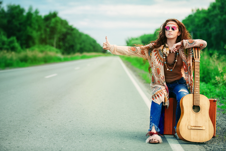 Hitchhiking girl. Beautiful hippie girl standing on a highway and catching a passing car. Spirit of freedom. Fashion shot. Bohemian, bo-ho style.の写真素材