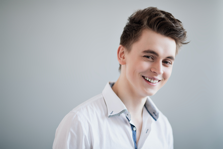 A portrait of a smiling young man wearing a white shirt and posing indoor. Men's beauty, fashion.の写真素材