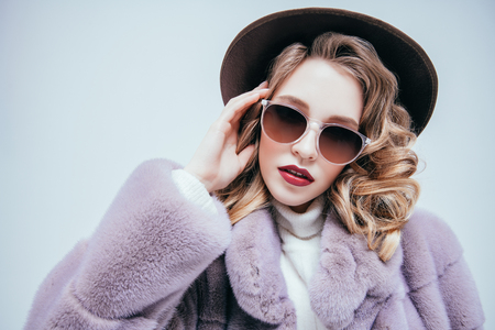 A portrait of a beautiful woman wearing a fur coat and a hat and sunglasses. Beauty, winter fashion, style.の写真素材