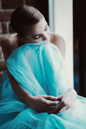 A portrait of a mysterious lady in a fluffy dress posing indoor on the windowsill. Fairy tale, fashion.の写真素材