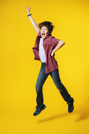 A full length portrait of a bright young boy jumping in the studio over the yellow background. Kids, fashion.の写真素材