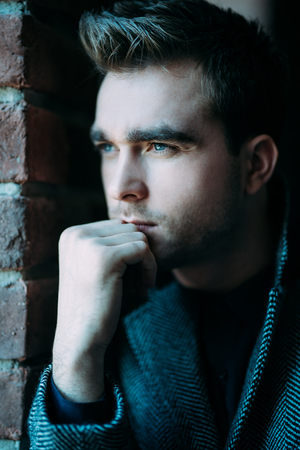 A close up portrait of a thoughtful fashionable young man near the brick wall. Casual fashion for men.の写真素材