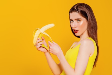A portrait of a bright beautiful girl with banana posing in the studio over the yellow background. Beauty, health.の写真素材