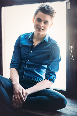 A portrait of a young man wearing a blue shirt and posing indoor. Men's beauty, fashion.