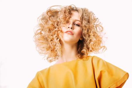 A portrait of a charming young girl with curly fair hair in a yellow dress. Fashion, beauty.の写真素材
