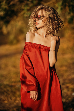 A portrait of a charming young girl with curly fair hair in a red dress. Fashion, beauty.の写真素材