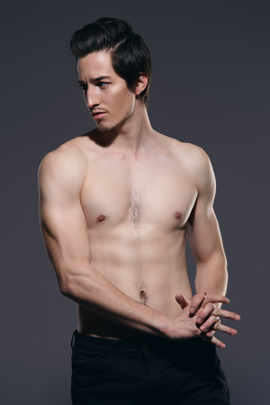 Portrait of a sexy young man with slender body posing at studio in jeans. Gray background. Men's health.の写真素材