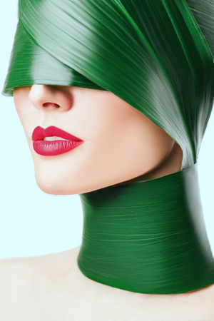 A close up portrait of a beautiful girl with a head rolled up in a leave posing in the studio over the white background. Beauty, nature, make up.の写真素材