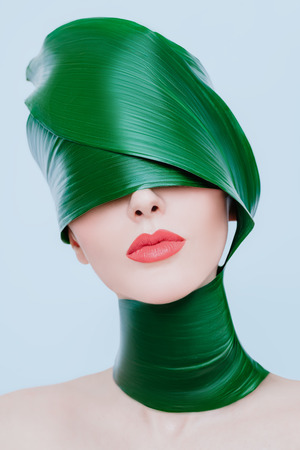 A close up portrait of a beautiful girl with a head rolled up in a leave posing in the studio over the white background. Beauty, nature, make up.の写真素材