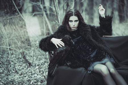A portrait of a beautiful mysterious girl in black posing on the armchair in the forest. Beauty, fashion, nature.の写真素材