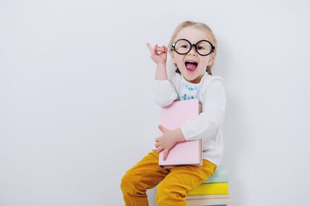 A portrait of a cute pretty girl wearing glasses sitting with textbooks over the white background. Beauty, fashion, school, education.の写真素材