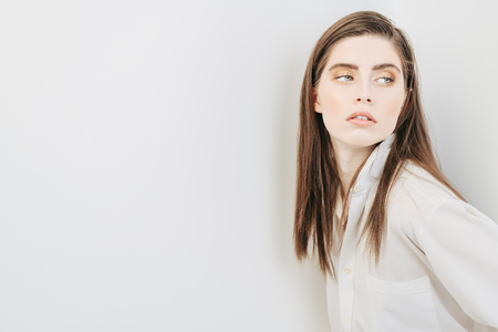 A portrait of a beautiful dark-haired young woman wearing a white shirt posing over the white background. Beauty, cosmetics, fashion.の写真素材