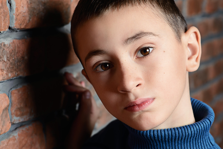 Portrait of a sad nine year old boy leaning against the brick wall. Clothes for children. Kid's fashion.の写真素材