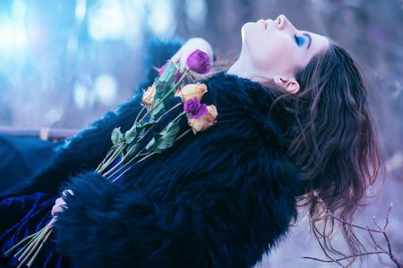 A portrait of a beautiful mysterious girl in black posing on the armchair in the forest with flowers. Beauty, fashion, nature.の写真素材