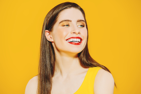 A close up portrait of a bright beautiful emotional  girl posing in the studio over the yellow background. Beauty, health.の写真素材