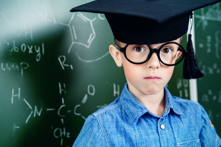 A portrait of a young boy in glasses posing over the blackboard at school. Education, knowledge.の写真素材