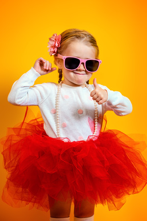 A portrait of a bright young pretty girl in skirt and sunglasses. Summer bright fashion for kids.の写真素材