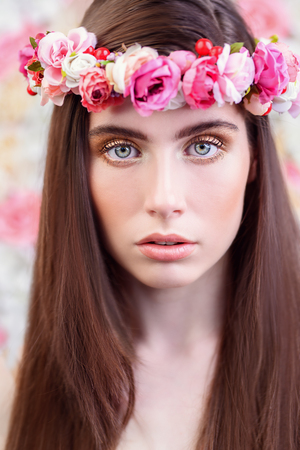 A close up portrait of a beautiful dark-haired young woman posing over the background with flowers. Beauty, cosmetics, flowers.の写真素材